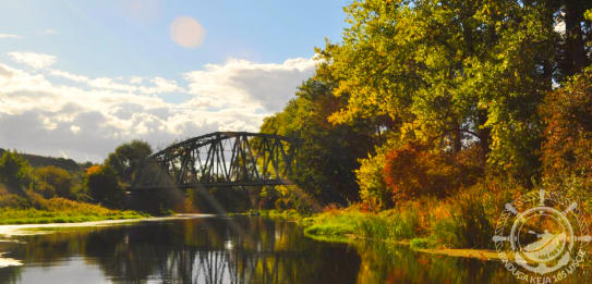 Spływy rzeka Notecia. Widok na most kolejowy w Ujściu. Ciepłe odcienie, rzeka skapana w blasku słońca.